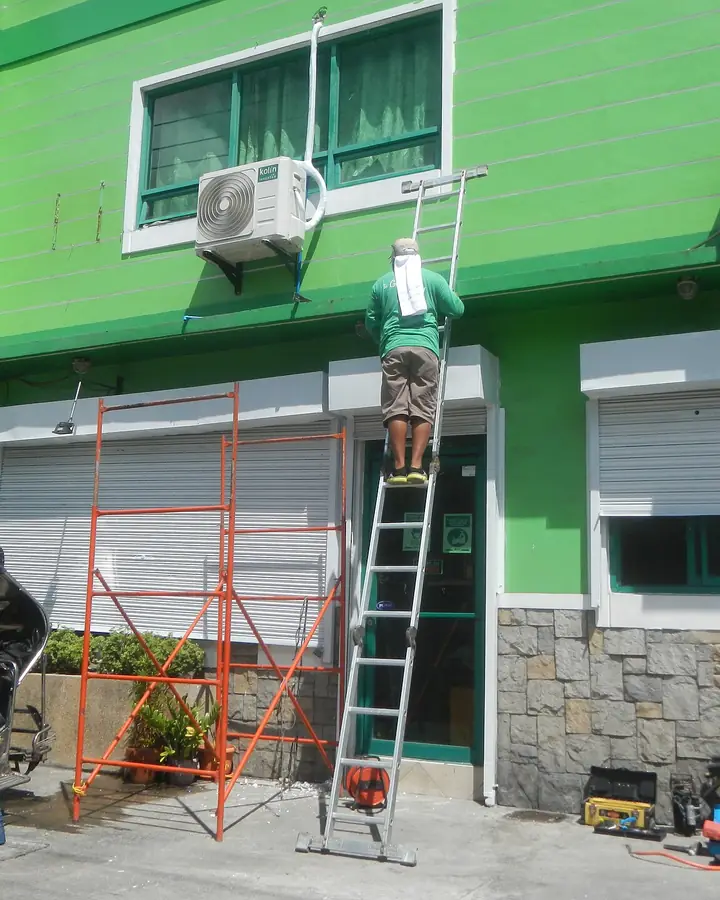Técnico en escalera instalando unidades de aire acondicionado en la fachada de un edificio